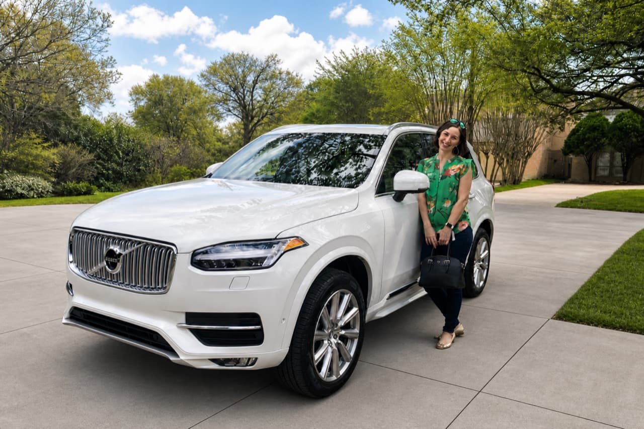 A smiling woman standing beside a white SUV in a driveway